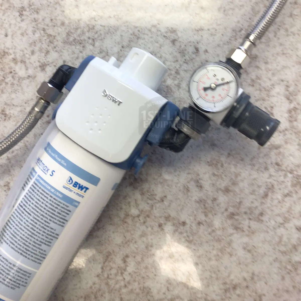 A BWT Bestmax Installation Kit with a pressure gauge is shown on a speckled countertop, featuring metal hoses for connection and components included for straightforward setup.