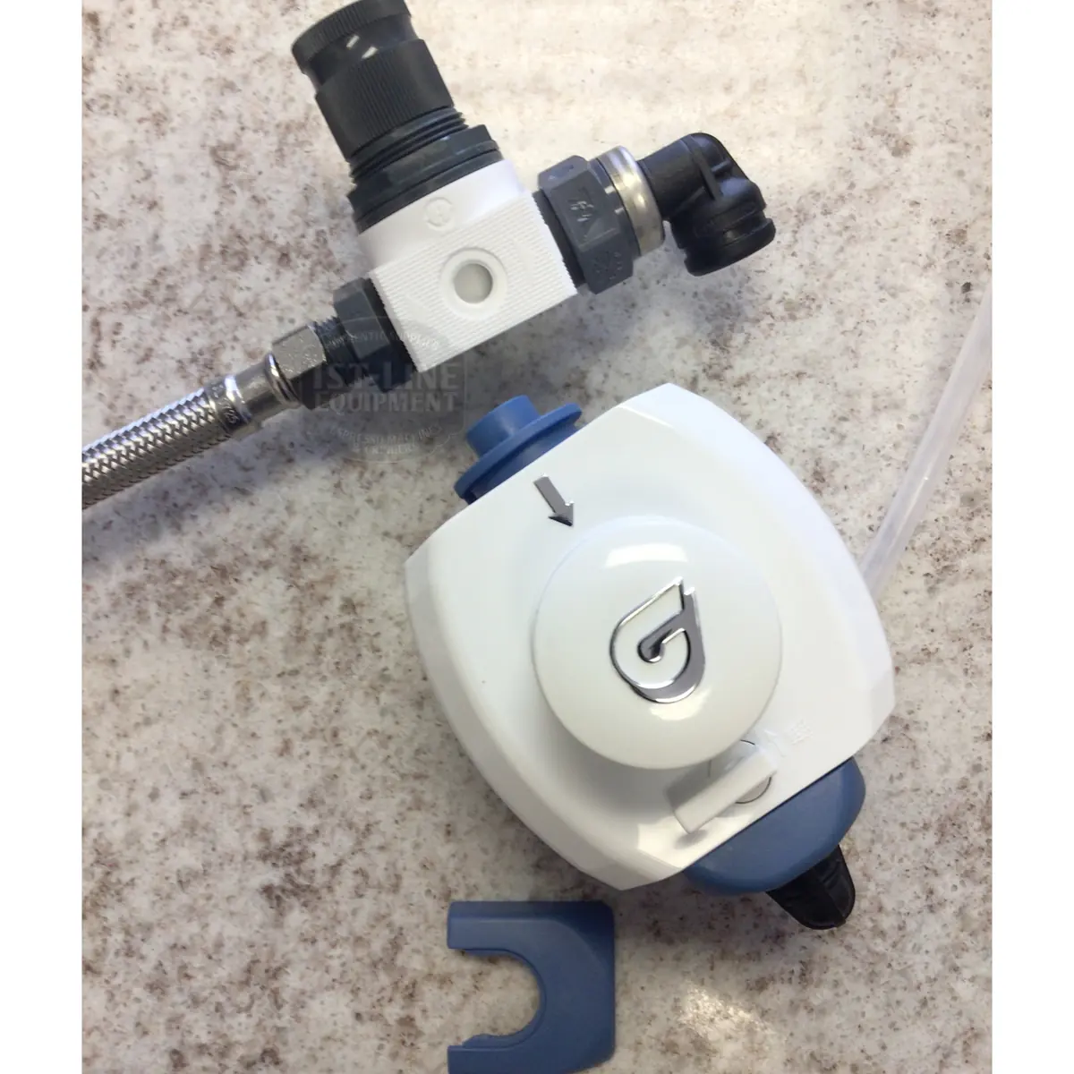 A close-up of a white and blue water filter valve from the BWT Bestmax Installation Kit, connected to a metal hose, with a plastic clip nearby on a speckled countertop.
