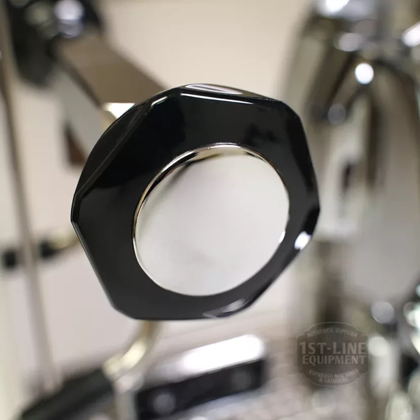 Close-up of the shiny black and chrome handle with a hexagonal end on the DISCONTINUED Profitec Pro 700 Dual Boiler Espresso Machine - PID, Switchable. Reflections highlight its metallic surface; blurred background shows machine details. © 2025 1st-line.com