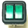 A close-up of the V.4411 GREEN DOUBLE SWITCH, a rectangular black plastic switch featuring two green illuminated buttons side by side, displayed from the front against an off-white background. © 2025 1st-line.com
