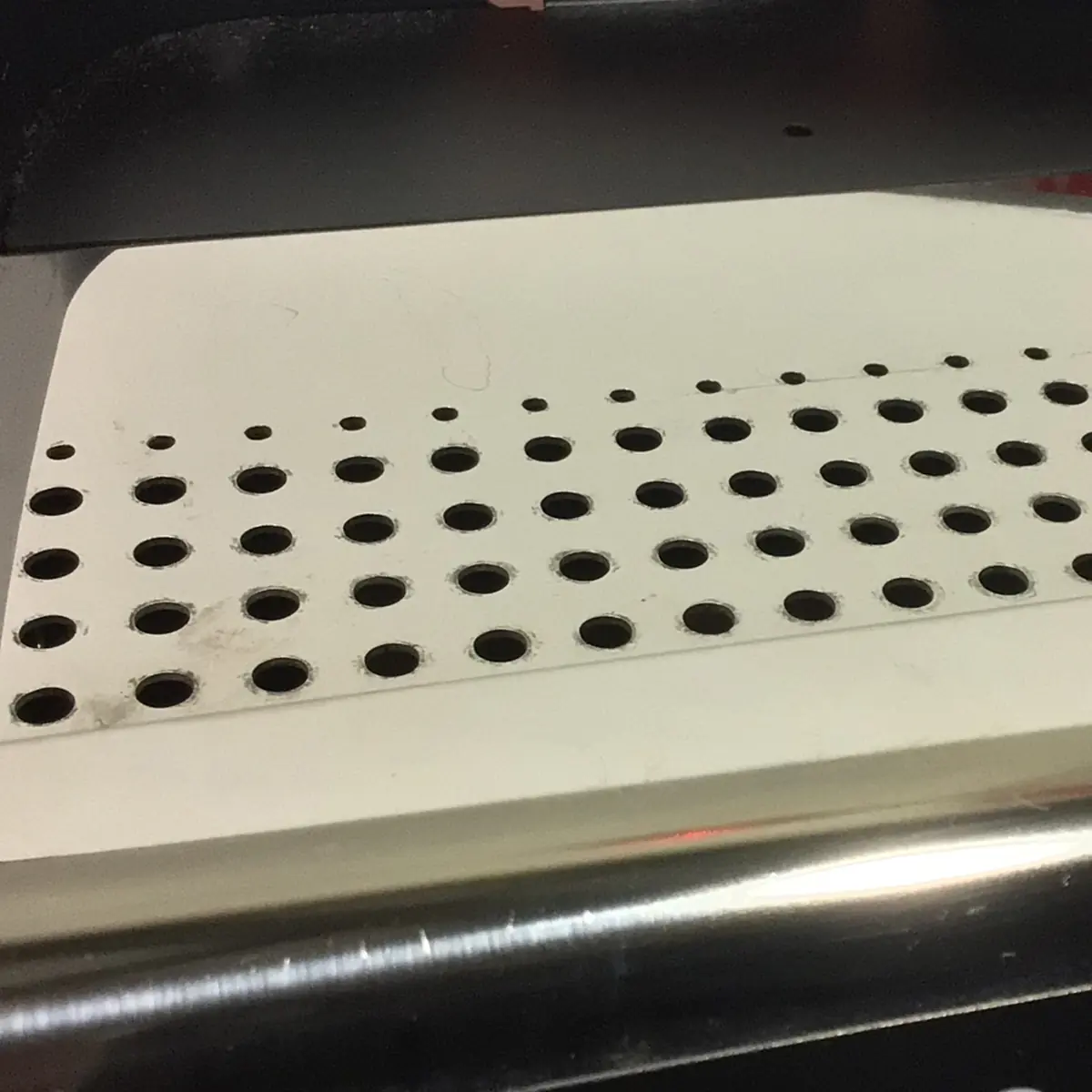 Close-up of a white metal surface with rows of round holes, likely part of the SIDEWALK SALE - VBM Domobar Super Analogic HX Espresso Machine OPEN BOX (E013), with a metallic edge visible in the foreground.