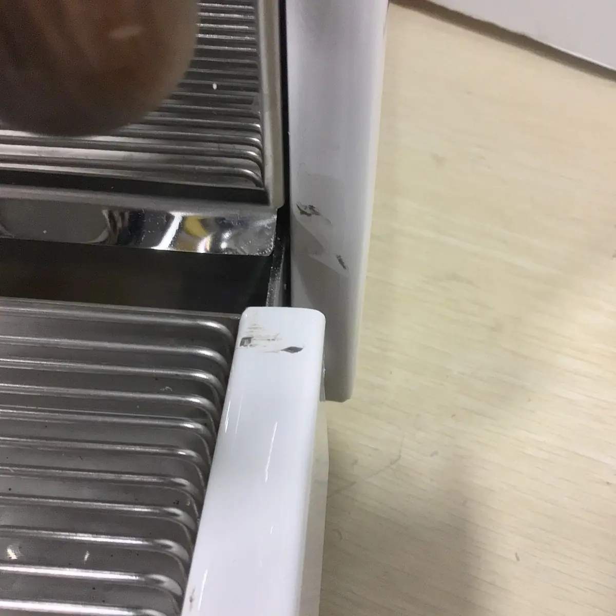 Close-up of a SOLD RETURNED & REFURBISHED Bezzera Aria HX Special Edition Espresso Machine w/ Flow Control (C104), showing scratch marks and scuffs on the white plastic part, placed on a light-colored wooden surface.