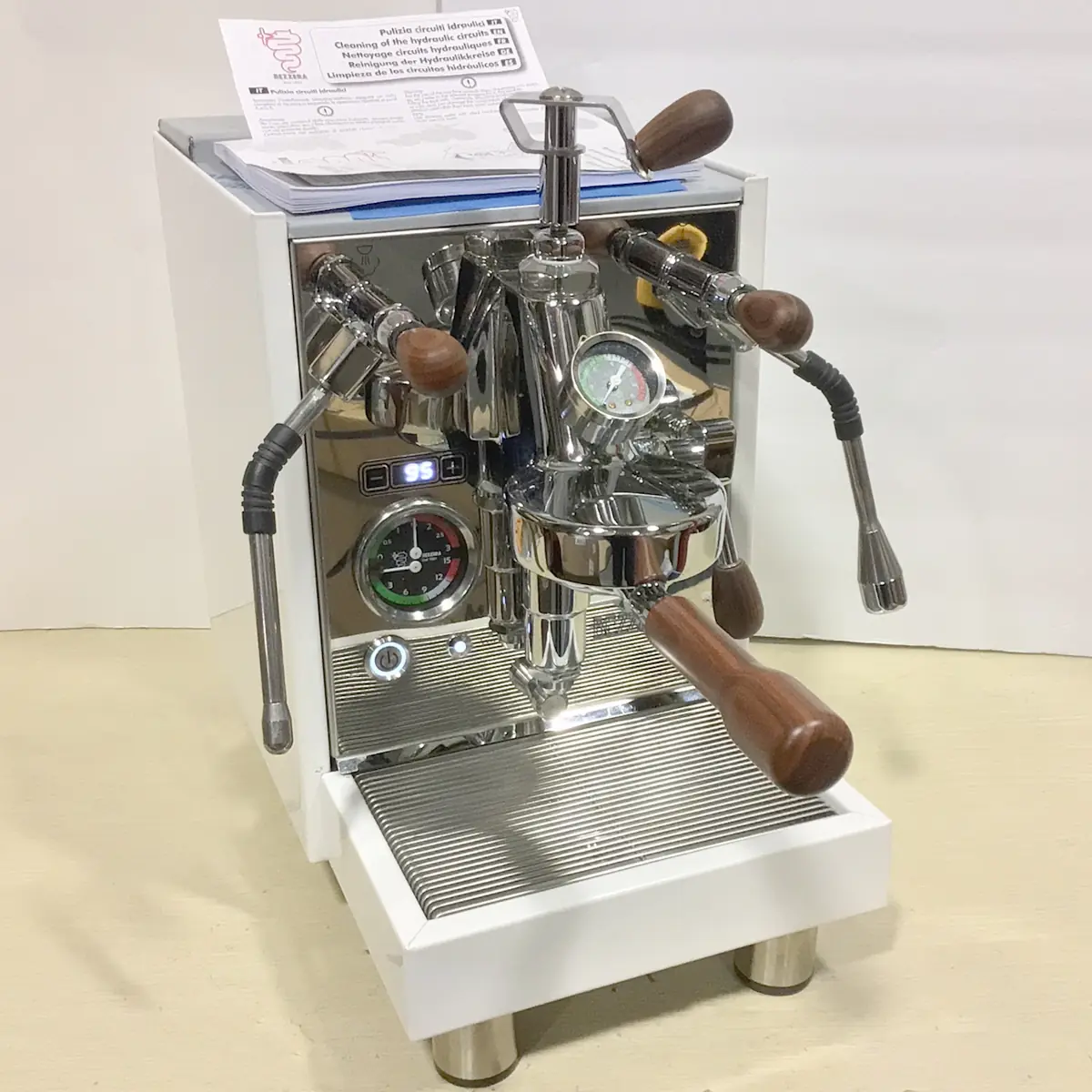 A SOLD RETURNED & REFURBISHED Bezzera Aria HX Special Edition Espresso Machine w/ Flow Control (C104) with wooden handles, pressure gauges, and steam wands sits on a light counter. Instruction papers rest on top; the plain background is light-colored.