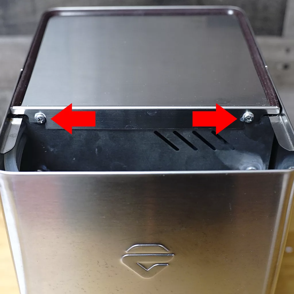 A close-up of a metal container with two red arrows pointing to screws on its top edge, indicating parts that may need to be unscrewed or removed. © 2025 1st-line.com