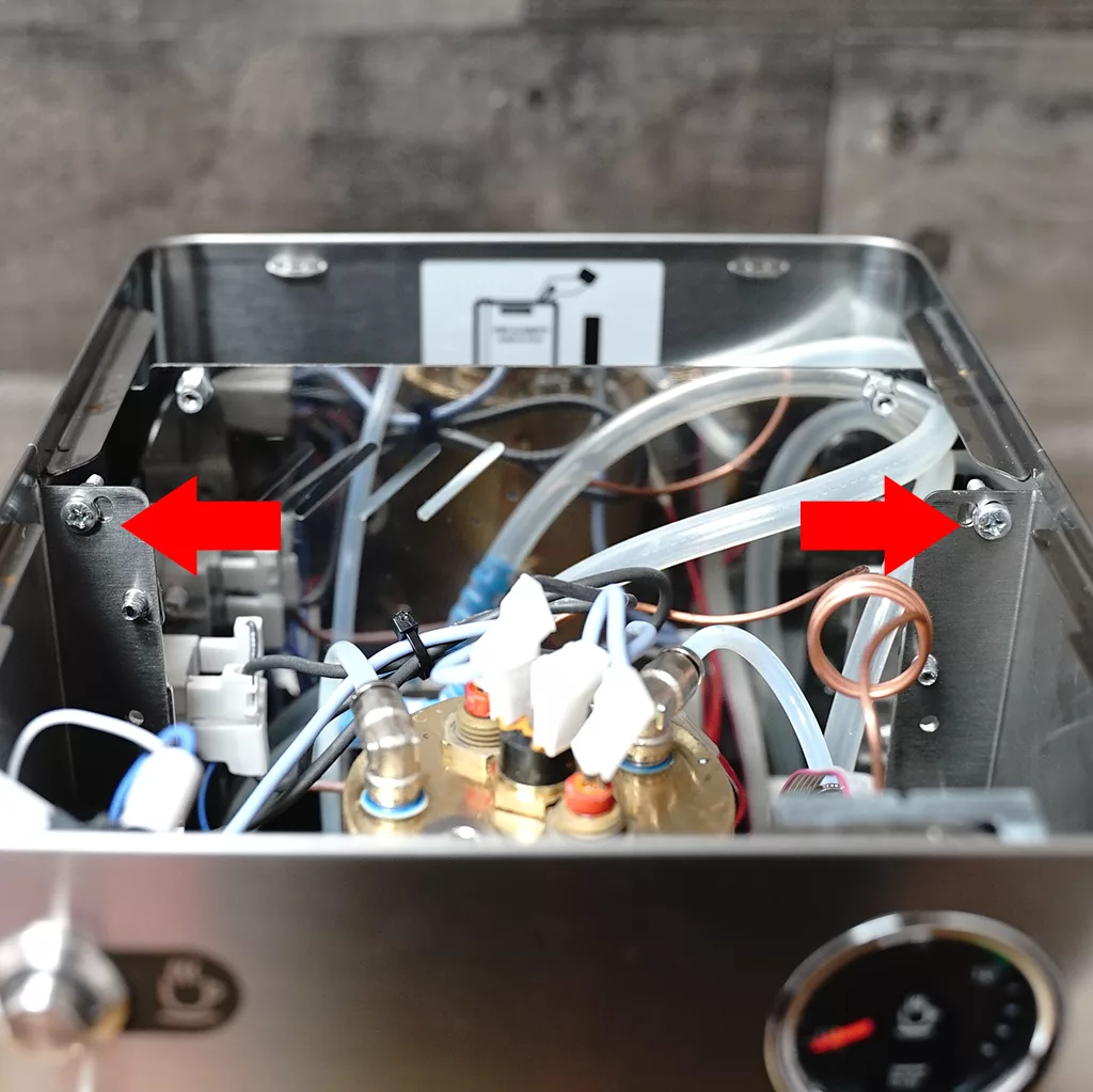 The inside of a coffee machine with exposed wires, tubes, and components; two large red arrows point to screws in the metal frame on either side. © 2025 1st-line.com