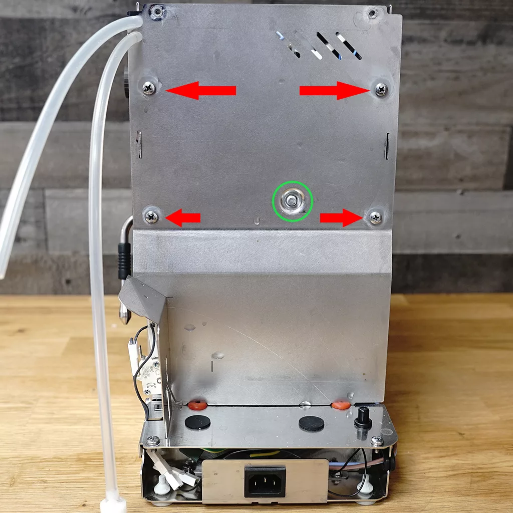 The back of a metal appliance, likely a coffee machine, is shown with four red arrows pointing to screws and a green circle highlighting a central screw. Tubes and wires are visible on the sides and bottom. © 2025 1st-line.com