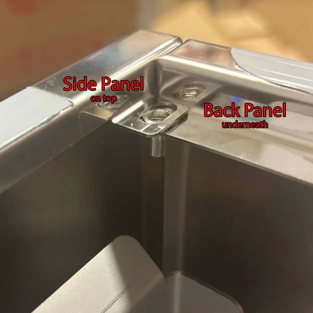 Close-up of metal panels joined at a corner on the Bezzera Sole, labeled “Side Panel on top” and “Back Panel underneath” in red text, showing how the panels overlap for accessing the inside during assembly.