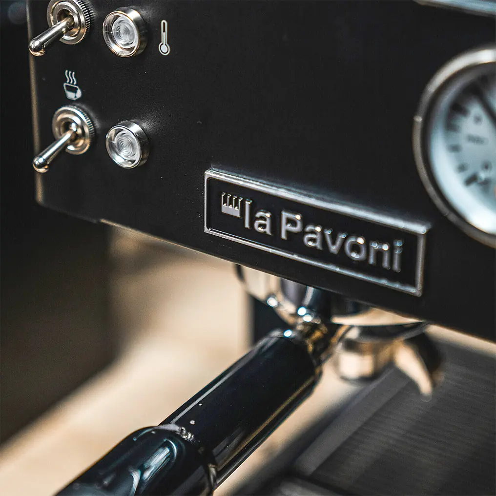 Close-up of the La Pavoni Casabar PID Espresso Machine, showcasing its control switches, pressure gauge, and portafilter handle attached under the machine.