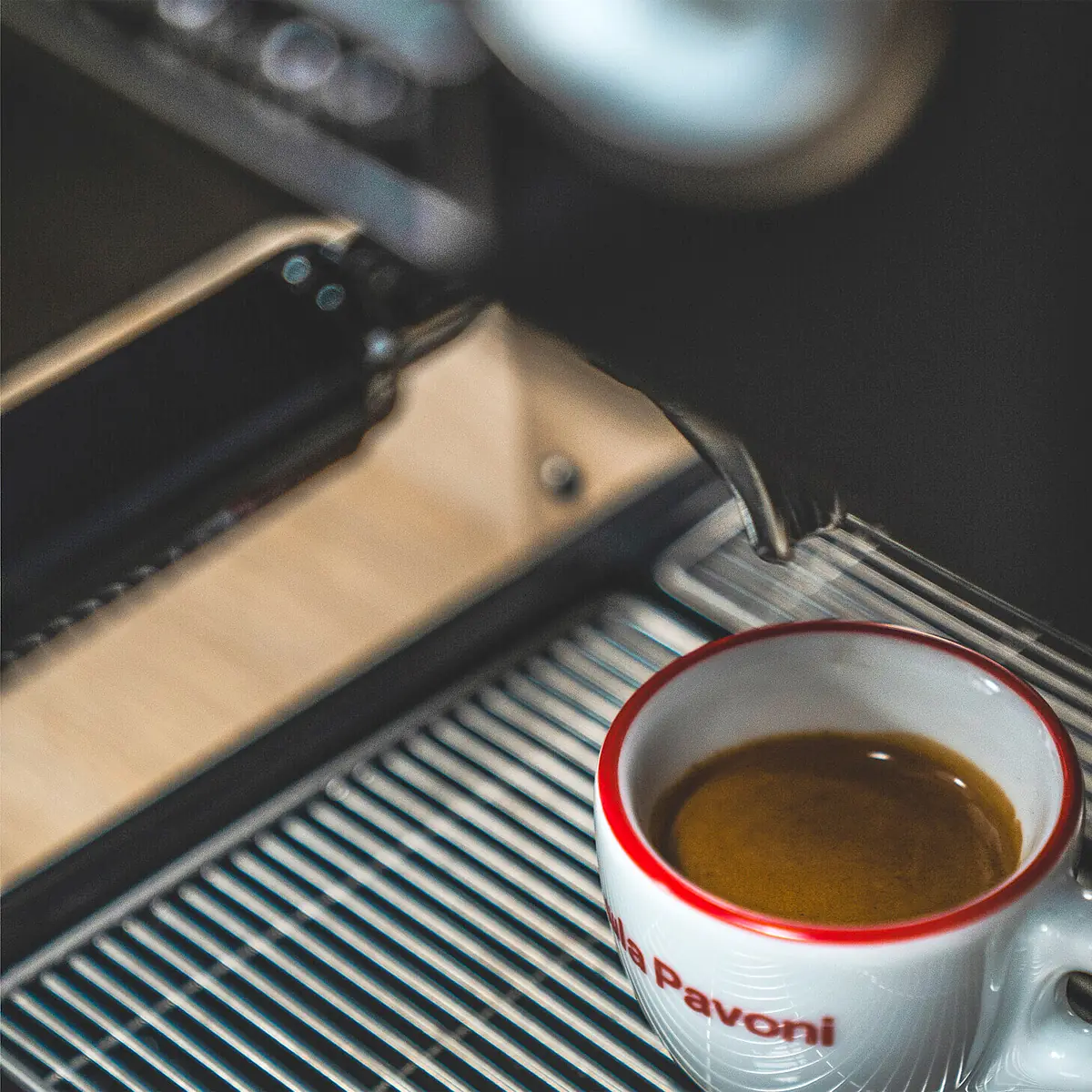 A close-up of the La Pavoni Casabar PID Espresso Machine pouring coffee into a white cup with a red rim, positioned on its metal drip tray.