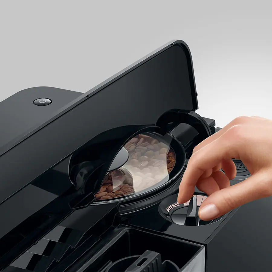 A hand adjusts a setting on the Jura C9 Super-Automatic Espresso Machine, which sits next to a see-through bean compartment filled with coffee beans.