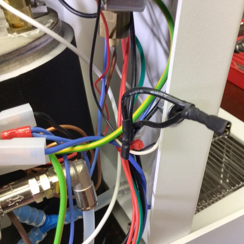 A close-up of various colorful electrical wires and connectors inside a Nurri R-Type machine, with some wires tied together and attached to metal and plastic components near the power button.