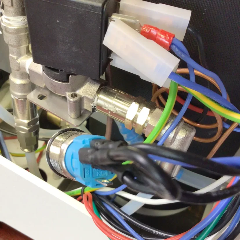 Close-up of an electrical component with multiple colored wires connected to metal parts and insulated terminals, likely part of a machine like the Nurri R-Type Dual Boiler. Plastic connectors may lead to the power button or other controls.