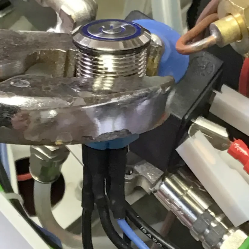 Close-up of metal pliers gripping a threaded cylindrical component with attached wires and electrical connectors, part of a mechanical or electronic device—possibly related to a Nurri R-Type dual boiler system.