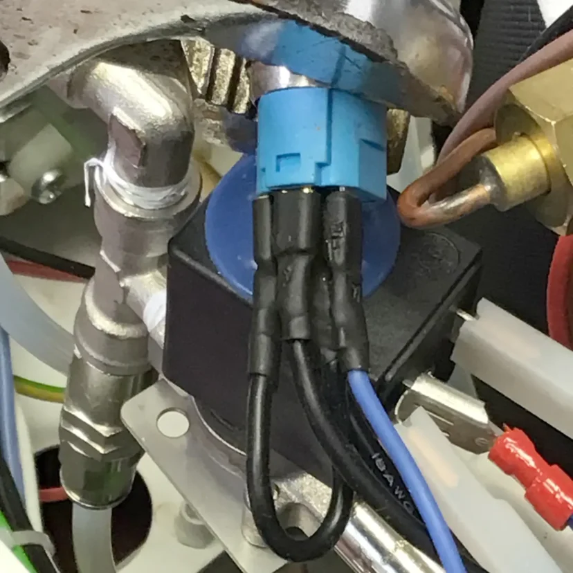 Close-up view of electrical wiring connected to a blue and black component, surrounded by pipes and metal fittings—possibly part of a Nurri R-Type dual boiler machine’s internal workings.