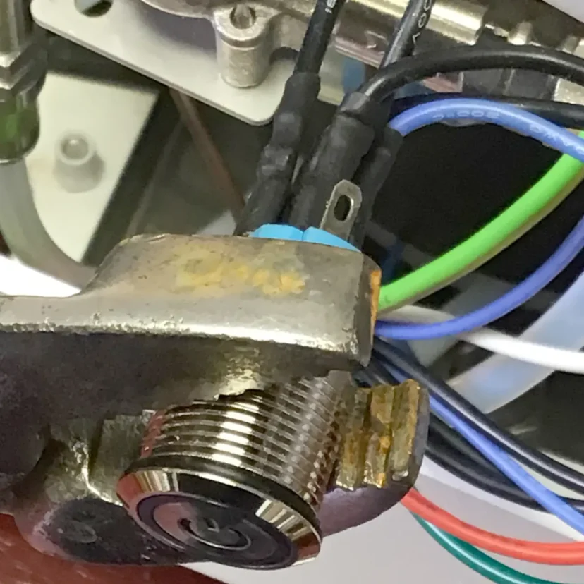 Close-up of a Nurri R-Type lock cylinder with wiring terminals attached, surrounded by green, blue, and white electrical wires, suggesting an electronic or mechanical component—possibly for a dual boiler or power button system.