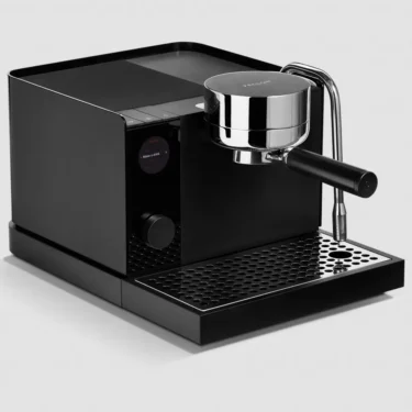 The Fellow Espresso Series 1 Espresso Machine, featuring a digital display, round portafilter handle, and metal steam wand, rests on a perforated drip tray against a light gray background.