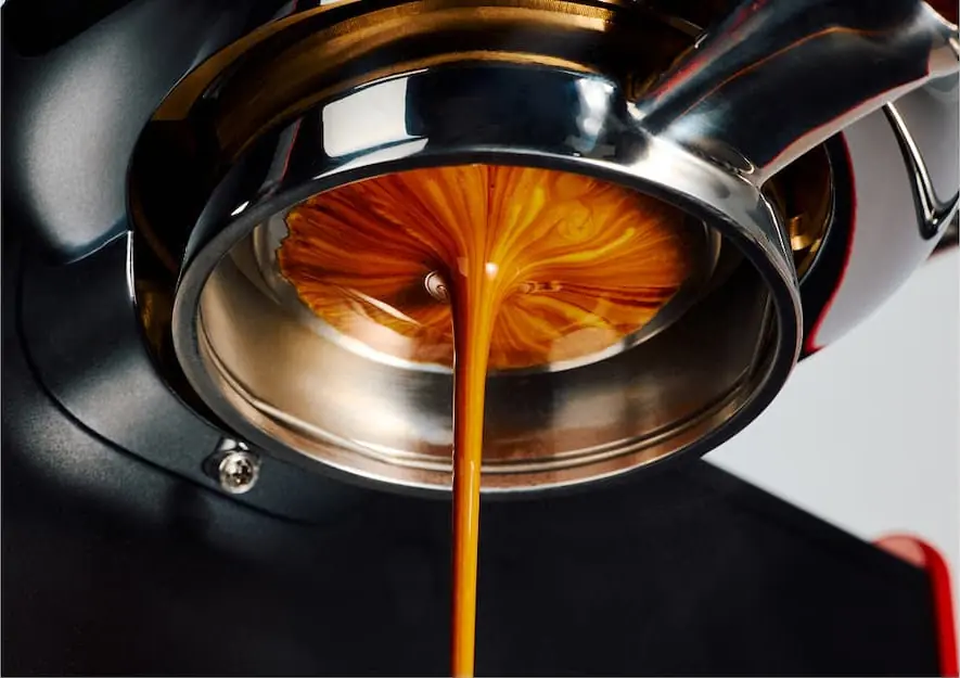 Close-up of espresso being extracted from a Fellow Series 1 Espresso Machine, with rich brown coffee and golden crema swirling as it flows into a cup below.