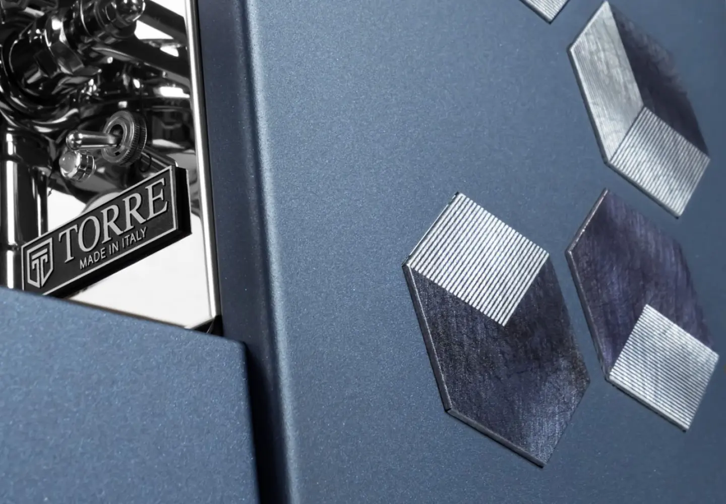 Close-up of a metallic blue surface with geometric hexagonal patterns and chrome detail reading "TORRE MADE IN ITALY," showcasing the modern, industrial design and luxury craftsmanship of the Torre Peppina Luxury Build.