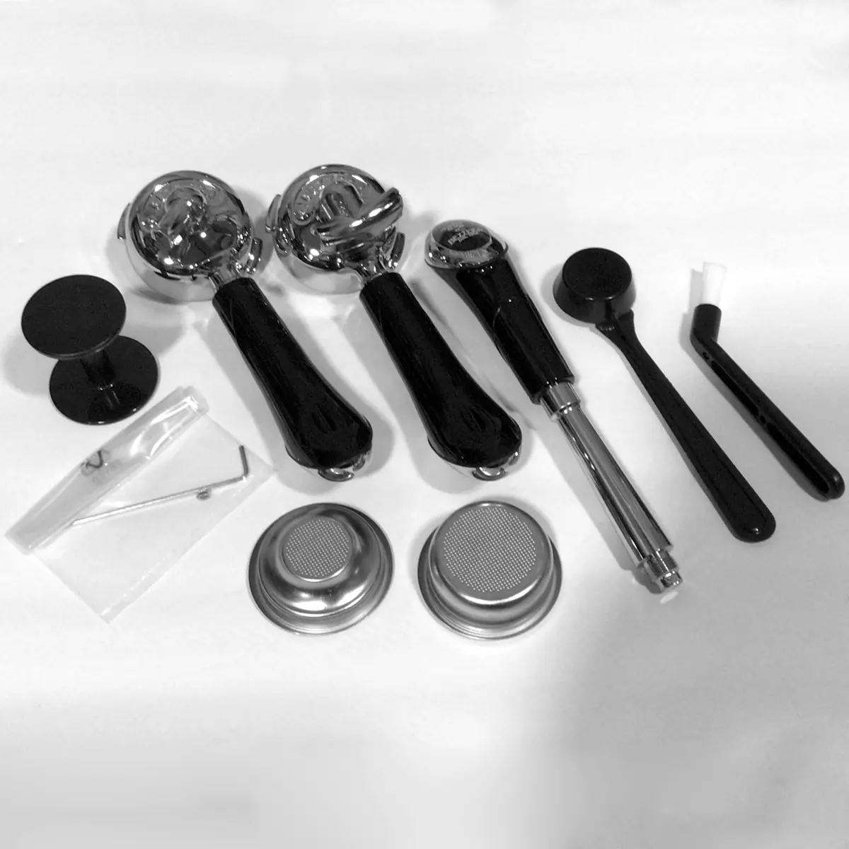 A set of accessories for the Bezzera Strega S Tank V2 Espresso Machine—three portafilters, two baskets, tamper tools, cleaning brush, dosing funnel, and black puck—are neatly arranged on a white surface.