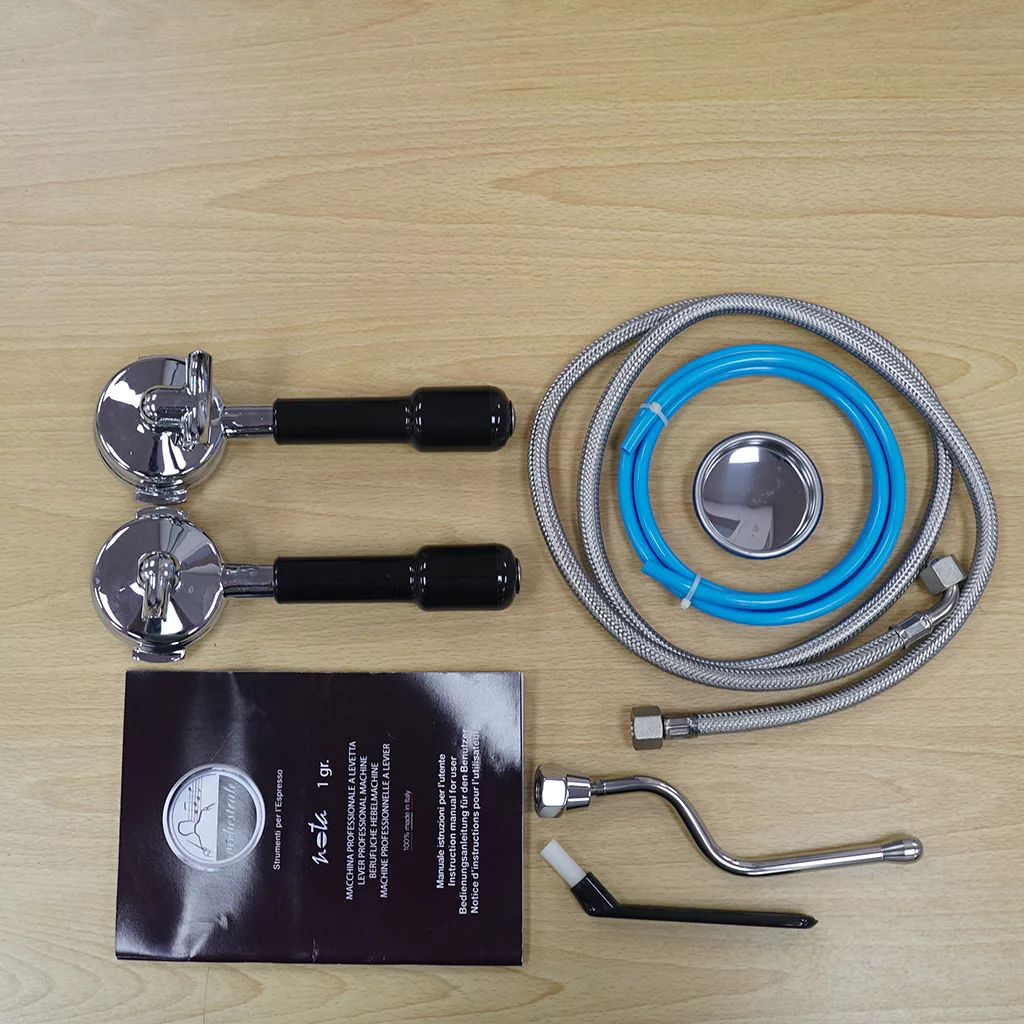 Sidewalk Sale: Orchestrale Nota White HX Espresso Machine (E111) parts, including two black-handled portafilters, a blue-silver hose, metal filter, spout, brush, and manual—ideal for completing your sidewalk sale discovery. © 2025 1st-line.com