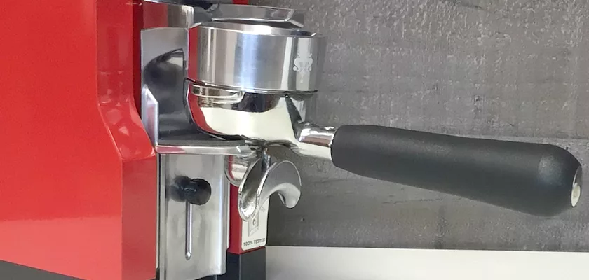Close-up of a red espresso machine with a black-handled portafilter against a gray background—perfect to pair with the Eureka Mignon Libra Espresso Coffee Grinder for precise, weight-based grinding.