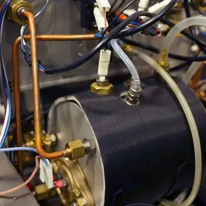 Close-up of mechanical and electrical components, including copper pipes, wires, connectors, and a cylindrical metal part—possibly part of Elektra Verve equipment used to prevent boiler overheating or manage coffee steam.