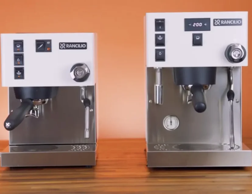 Two silver and white Rancilio espresso machines—a Silvia Pro X and a Silvia Classic—are side by side on a wooden surface with an orange background, each featuring control buttons and steam wands.