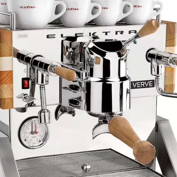 Close-up of a shiny Elektra Verve espresso machine with wooden handles, green red lights alternating near the pressure gauge, and several white Elektra-branded cups stacked on top.
