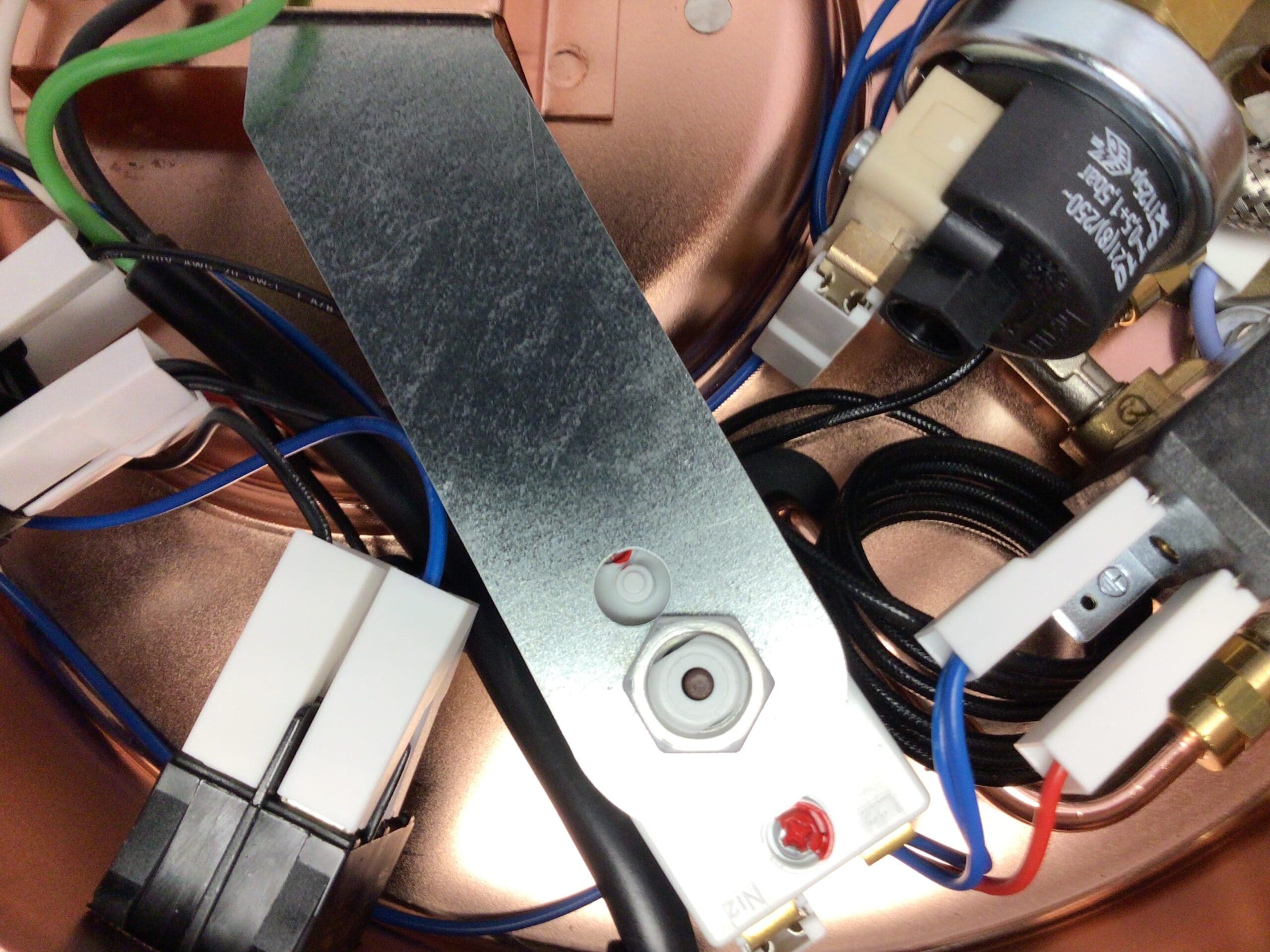 Close-up of electrical components inside an Elektra Semiautomatica device, showing wires, connectors, and a metal plate with labeled buttons and indicator lights. Copper and plastic materials are visible in the background. © 2025 1st-line.com