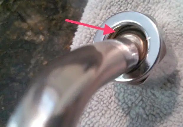 A close-up of a metal pipe connected to a fixture, with a red arrow pointing to a gap at the base, possibly indicating a Steam Valve Leak or installation issue. The fixture is set on a textured white surface. 2025 1st-line.com