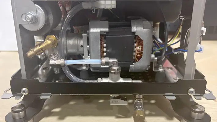 Close-up view inside a Bezzera Sole PID HX Espresso Machine, displaying metal parts, wiring, a blue tube, and a "TANK" label near two metal valves at the bottom.
