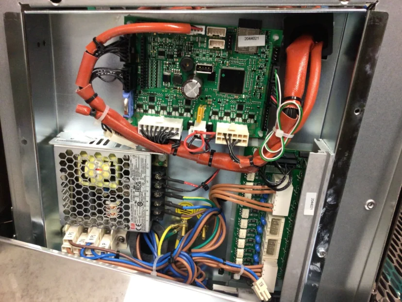 An open electronics panel reveals a Faema Board with circuit boards, red and orange cables, a power supply unit, and various wires connected to terminals inside a metal enclosure.