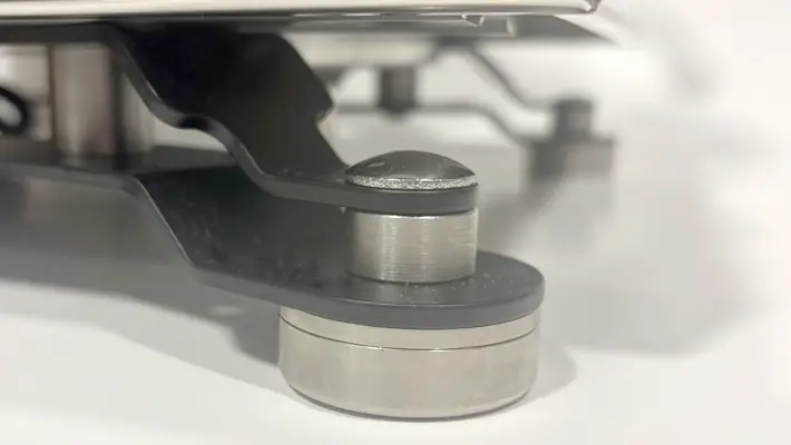 Close-up view of a metallic and plastic mechanical part, possibly a support or hinge, with cylindrical and flat components on a white surface.