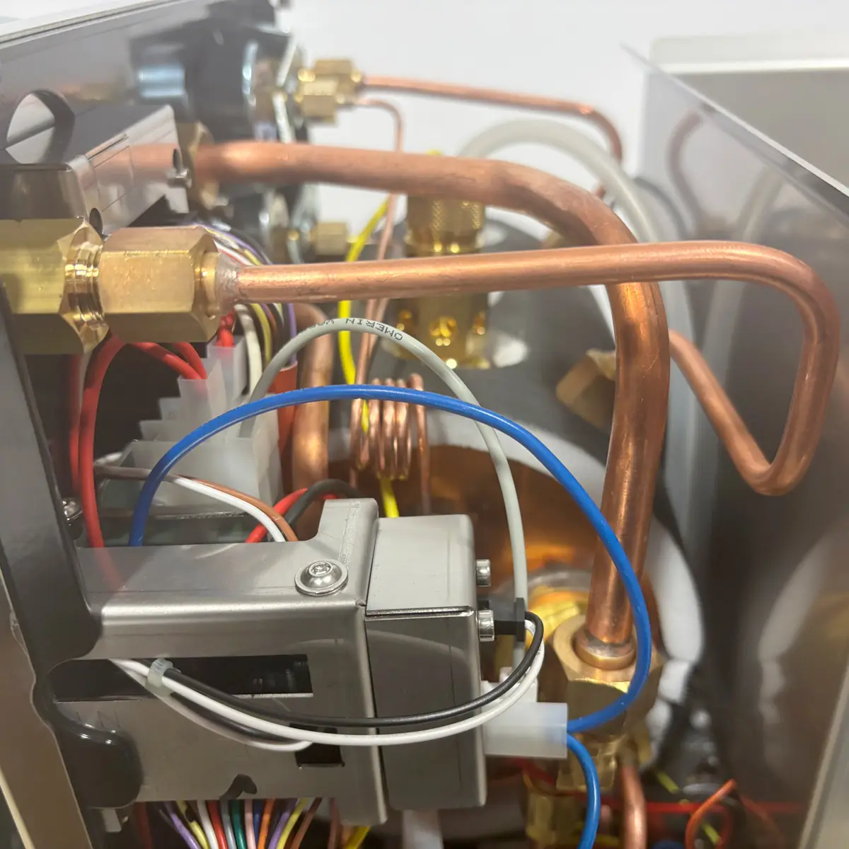 Close-up view of the internal components of a machine, showing copper pipes, wiring, and electrical parts inside a metal frame. The scene highlights the complex engineering of the device.