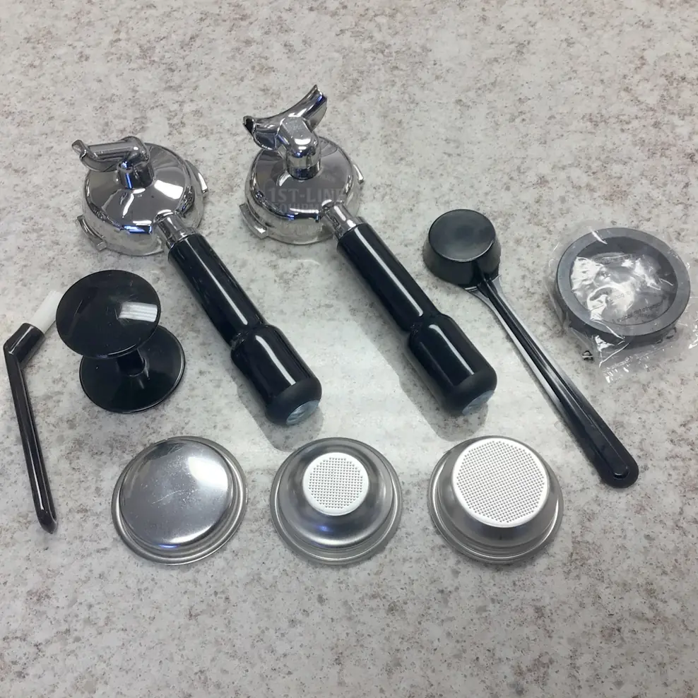 Various espresso machine accessories—including portafilters, a tamper, cleaning brush, dosing ring, and metal filter baskets—arranged neatly on a countertop, ideal for your La Pavoni Botticelli Evolution Dual Boiler Espresso Machine w/ Flow Control.