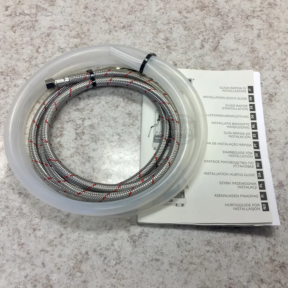 A braided metal hose and a clear plastic hose sit on a speckled countertop beside a multilingual guide for the La Pavoni Botticelli Evolution Dual Boiler Espresso Machine w/ Flow Control.