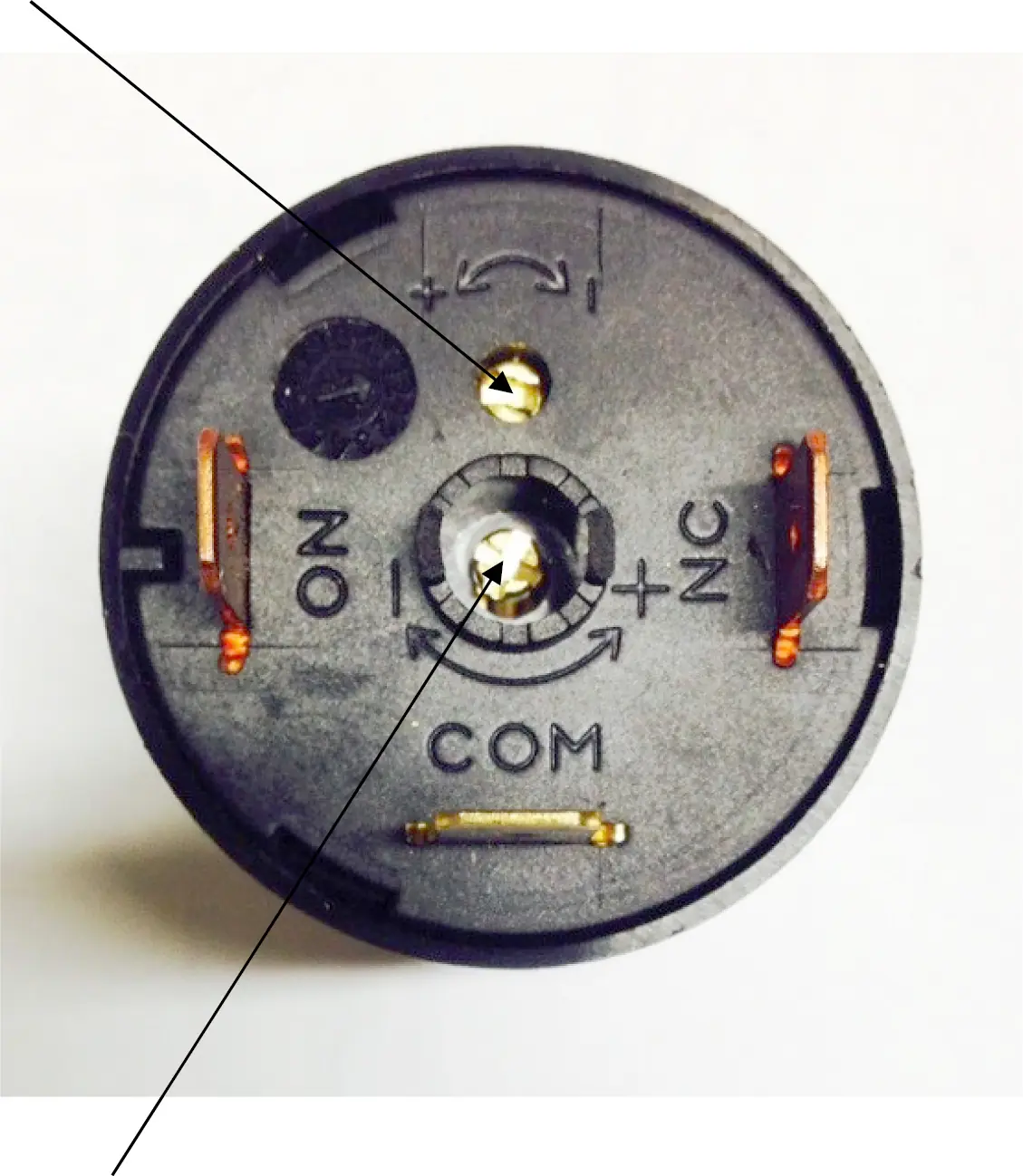 Close-up of a Ventus 110V pressurestat electrical component with labeled terminals: NO, NC, +, -, and COM. Two metal connectors and a central mounting hole are visible, with setting indicators and symbols on the surface.