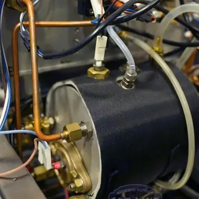 Close-up of industrial machinery showing metal pipes, wires, and connectors attached to a cylindrical component, likely part of an Elektra Verve steam boiler or espresso system that may be experiencing a not heating issue.
