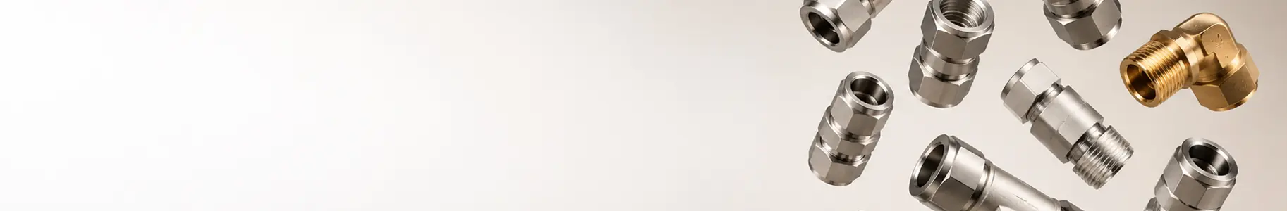 Several shiny metal fittings and one brass elbow fitting are arranged on a light background, with ample empty space on the left side of the image.
